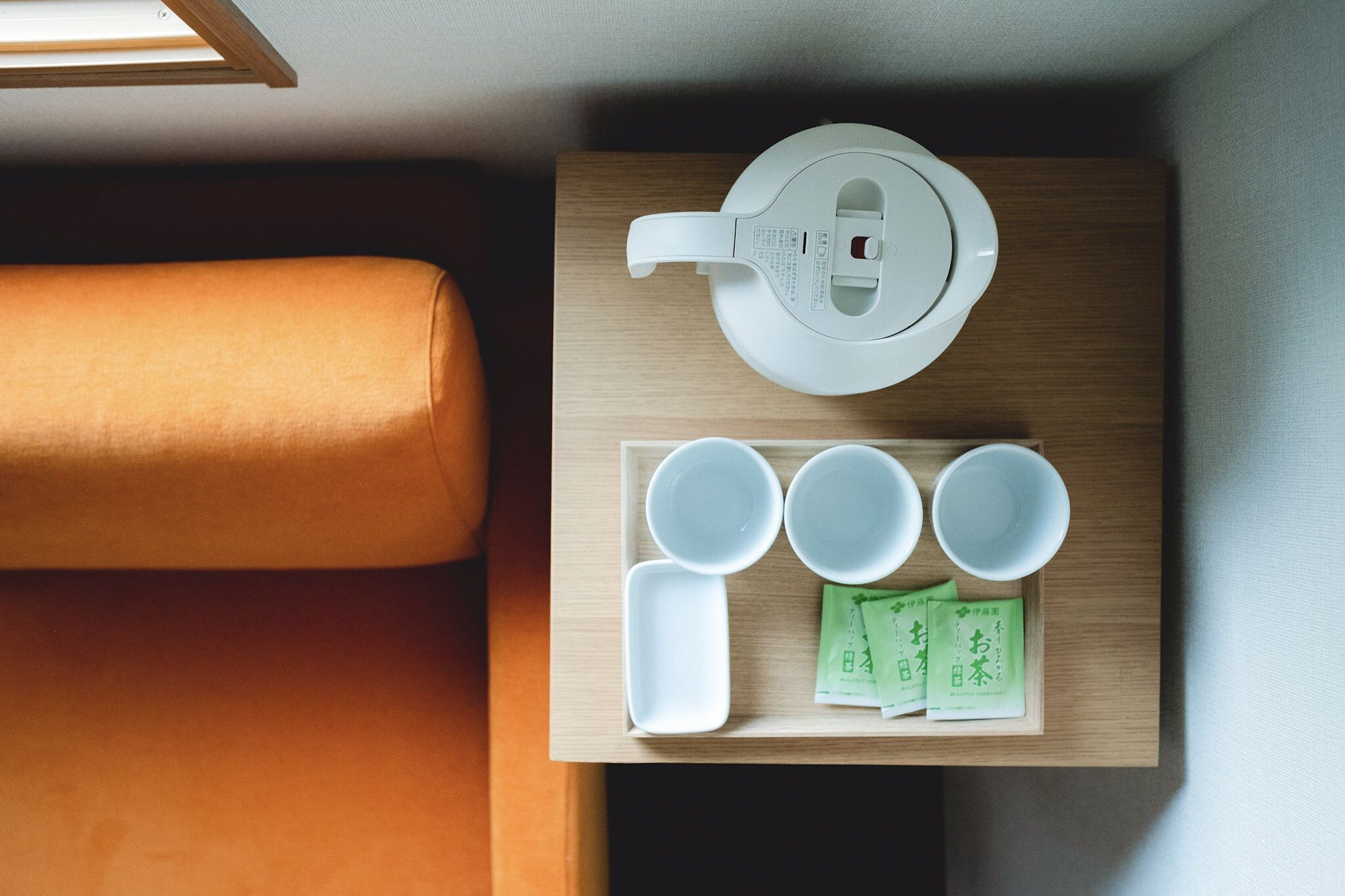 A top-down view of a room with a wooden table holding a white kettle, four white cups, and three green tea packets.