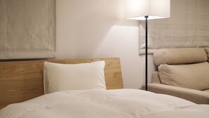A neatly made bed with white bedding, a wooden headboard, a bedside lamp, and a beige sofa with cushions. - So Kyoto Fushimi Inari (Kyoto)