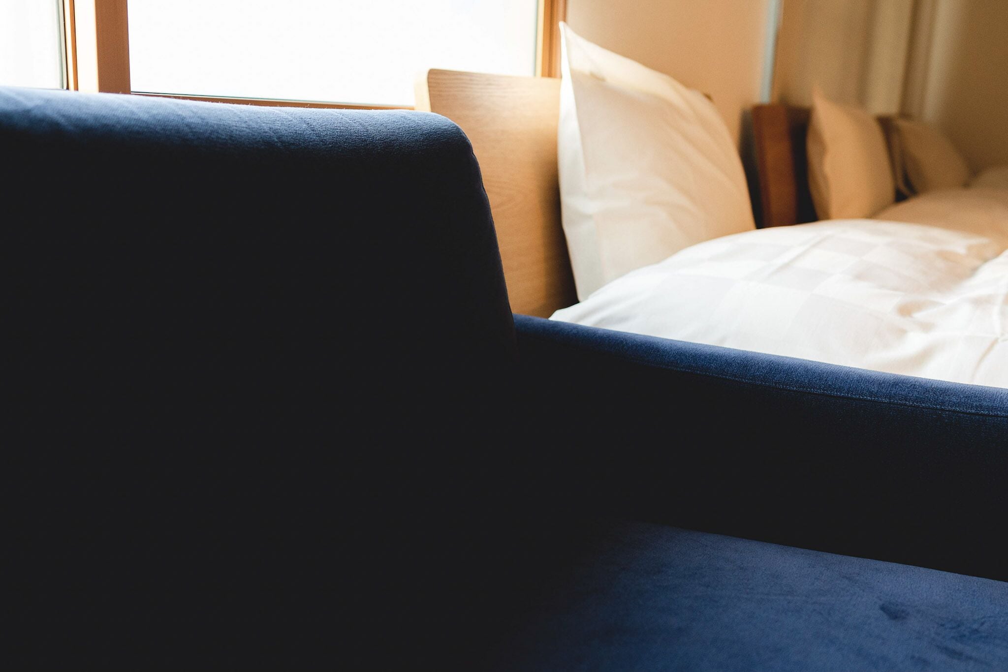 A hotel room with a bed, a window, and a blue armchair.
