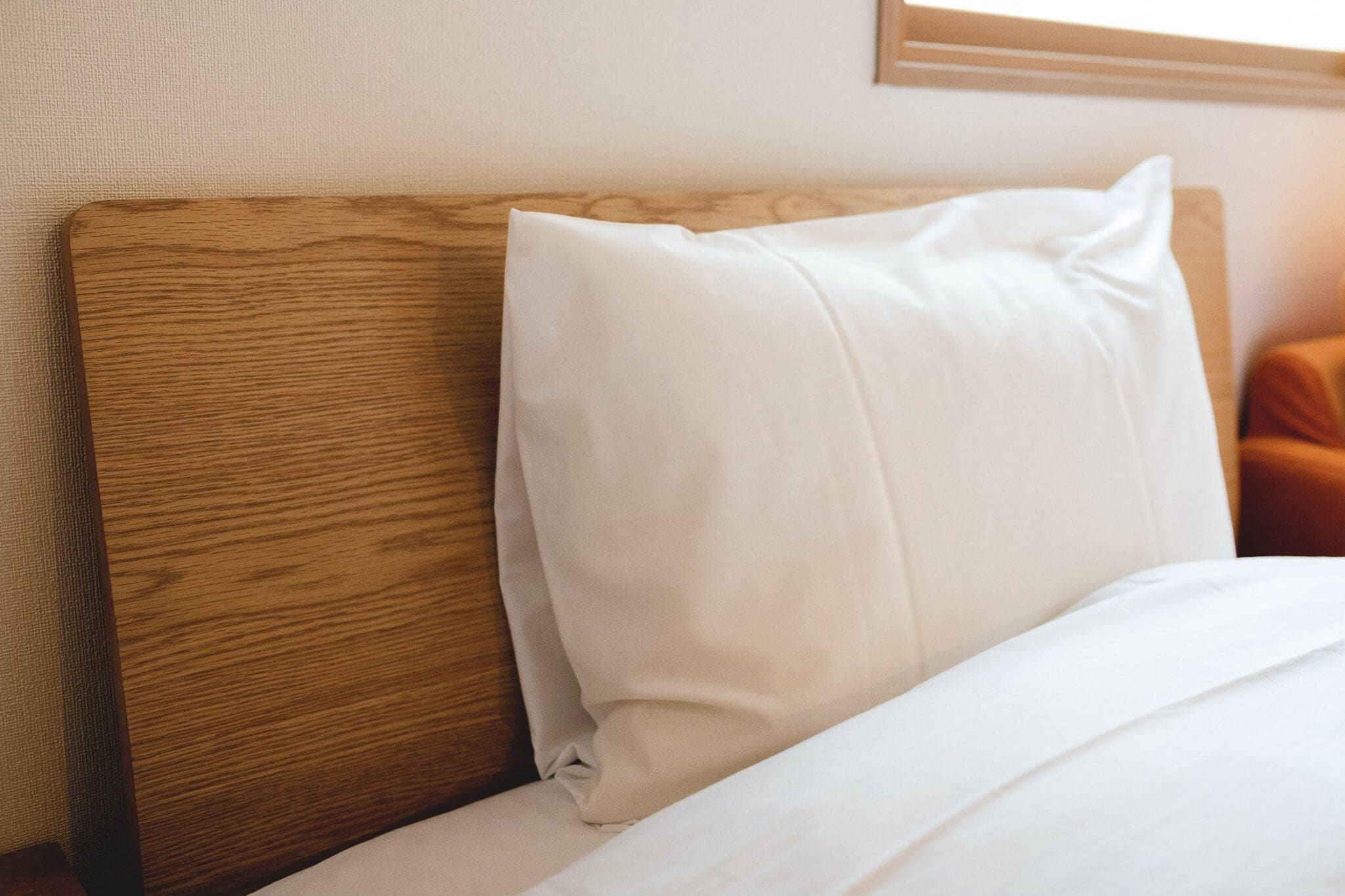 A wooden headboard with a white pillow and a white bedspread.