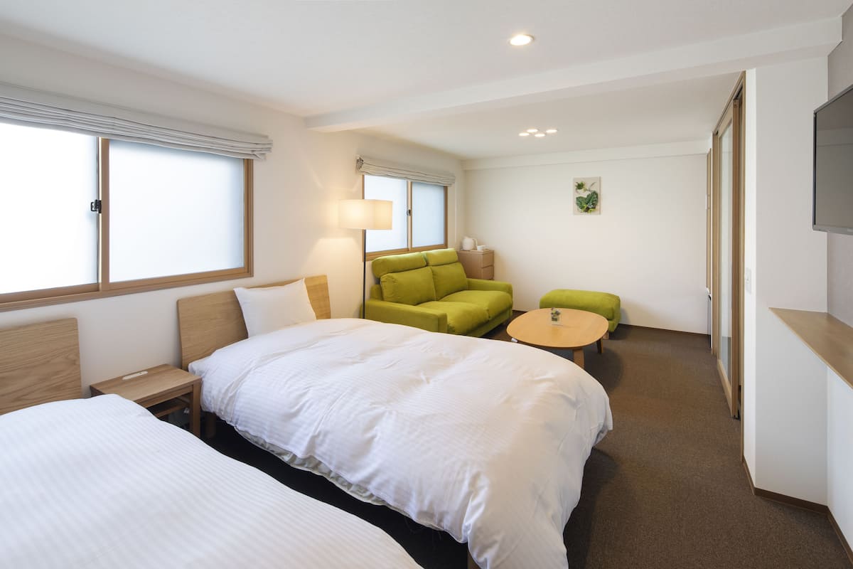 Habitación de hotel con una cama grande, un sillón verde, una mesita redonda y un televisor montado en la pared.