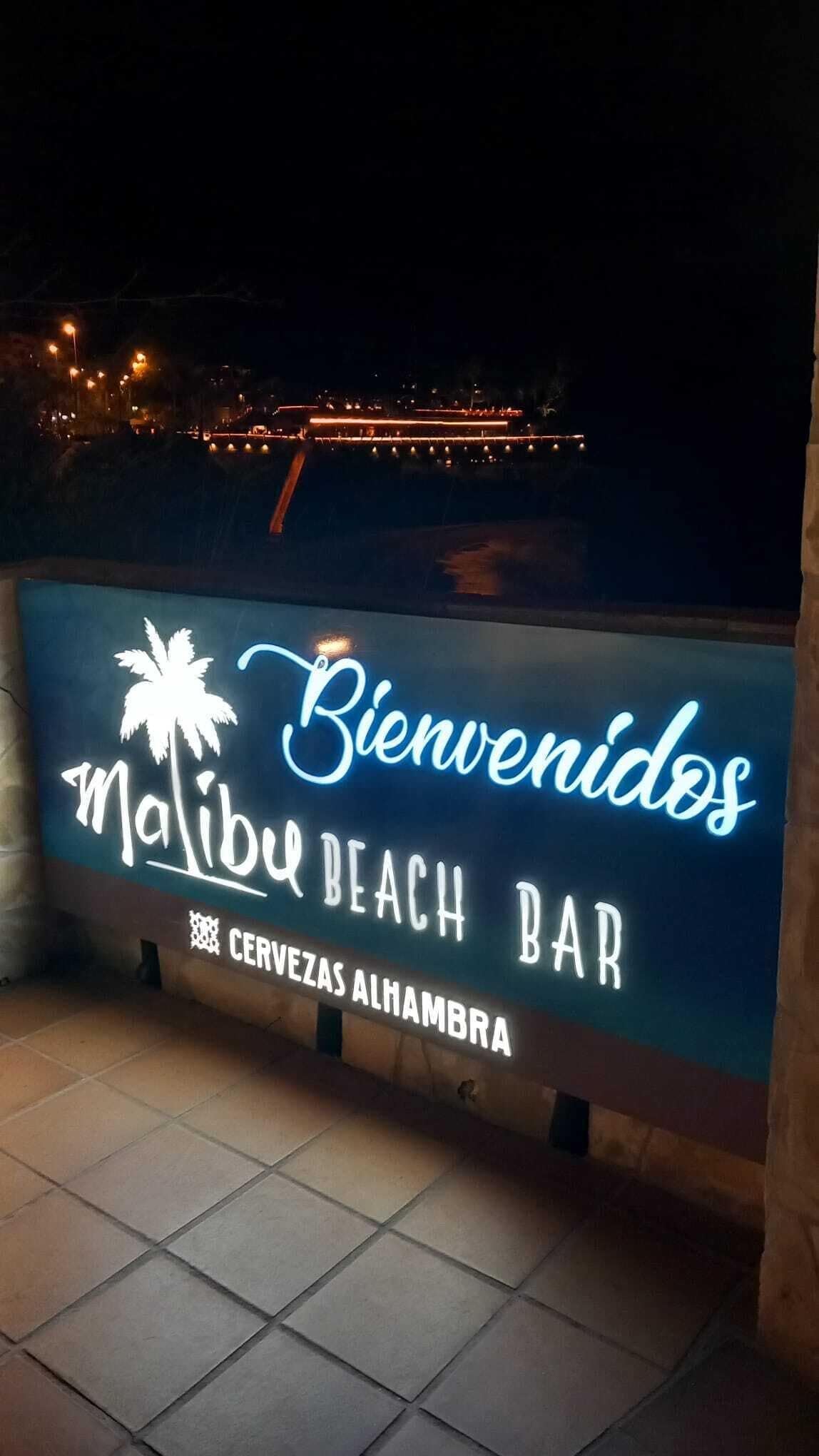 Señal de neón para el bar Malibu Beach, con una palmera y el texto 'Bienvenidos' y 'Cervezas Alhambra'.