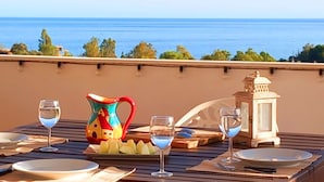 A table set for two with plates, glasses, a pitcher, and a lantern, overlooking a body of water.