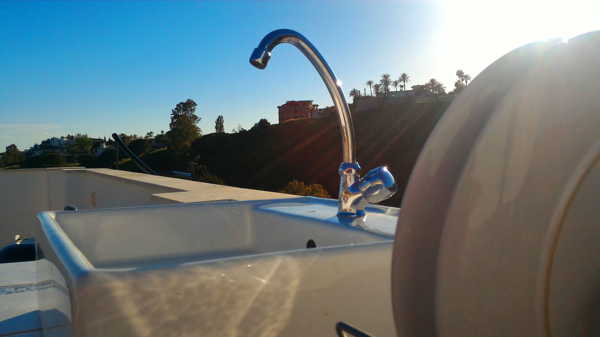 Un baño con un lavabo y grifo modernos, una vista despejada del paisaje circundante y un edificio al fondo.
