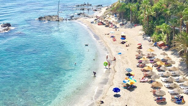 A beach with clear blue water, numerous umbrellas, and people enjoying the sun.