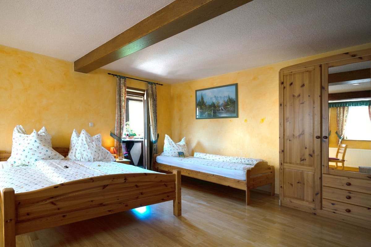 A room with two wooden beds, a nightstand with a lamp, a wooden wardrobe, and a painting on the wall.