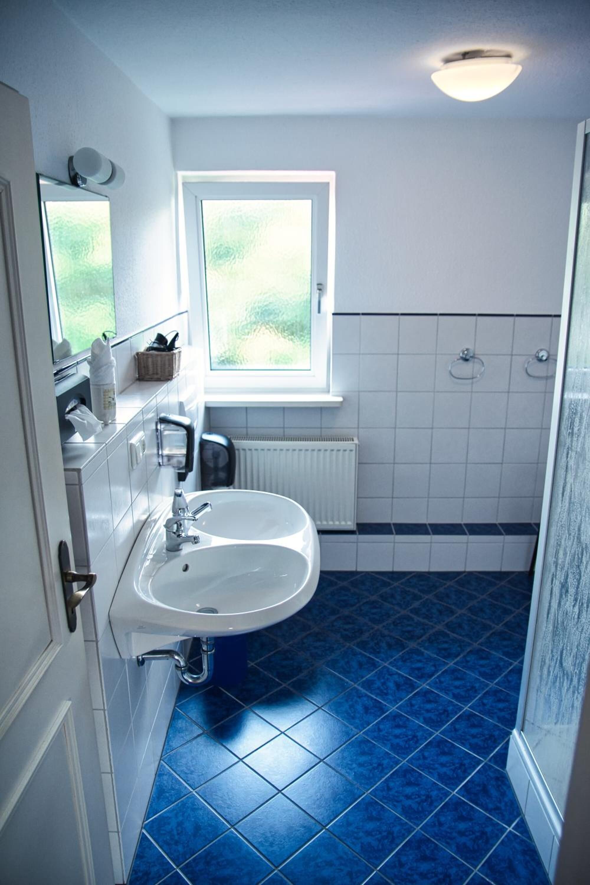 Un baño con lavamanos blanco, azulejos azules, una ventana y un radiador blanco.