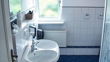 Un baño con lavamanos blanco, azulejos azules, una ventana y un radiador blanco.