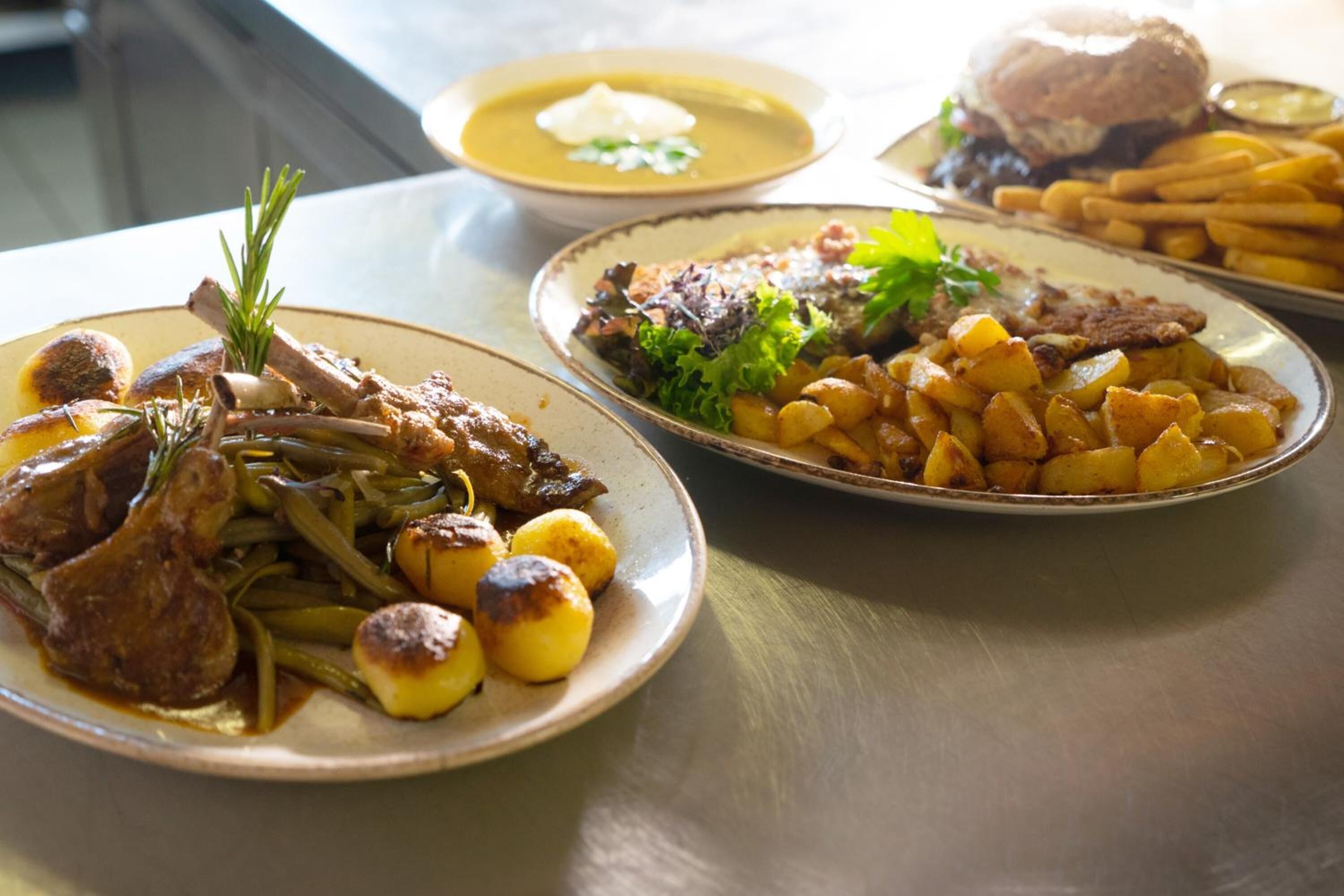 Una mesa con tres platos de comida: uno con carne asada y patatas, otro con ensalada y patatas fritas, y un tercero con una hamburguesa y patatas fritas.