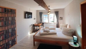 Un dormitorio con una cama de madera, una estantería, un escritorio y un televisor.