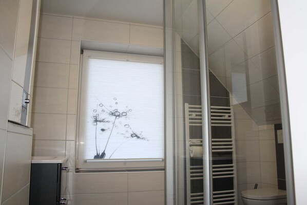 Un baño con ducha, inodoro, ventana con persianas y un perchero para toallas.