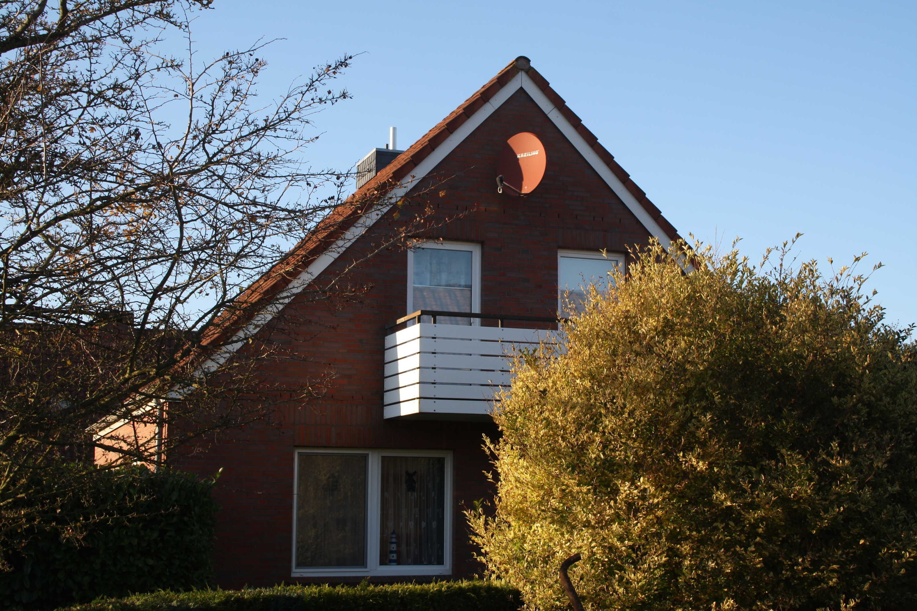 A two-story house with a red brick facade, white window frames, and a small balcony.