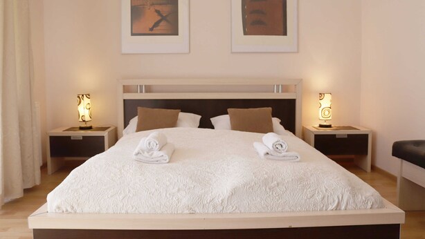 A neatly made bed with white linens and two towels, a wooden headboard, two bedside tables with lamps, and two framed artworks on the wall. - Bryza (CH18B) - CH18B (Swinoujscie)