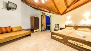 A bedroom with a wooden ceiling, a bed with floral bedspread, a sofa with striped cushions, and a television on the wall. - Harmony Hotel (Zakynthos)