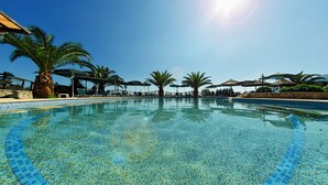 A clear blue swimming pool with palm trees and umbrellas, surrounded by a stone wall and a clear sky. - Harmony Hotel (Zakynthos)