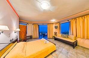Habitación de hotel con cama, sofá, balcón con mesa y sillas, y vista al mar.