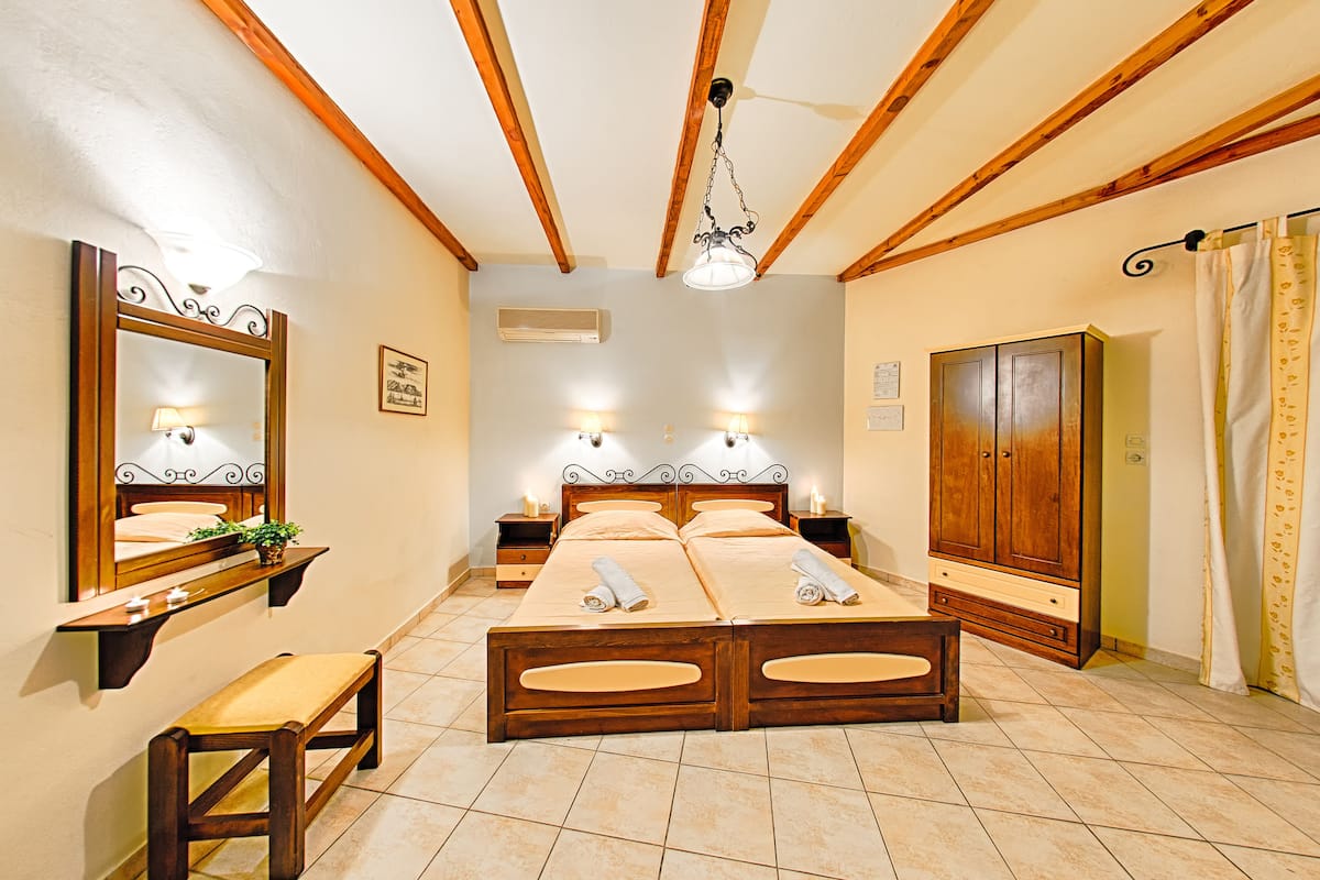 A double bed with a wooden frame, two bedside tables with lamps, a bench, a wardrobe, and a ceiling fan.