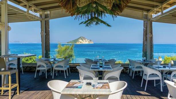 An outdoor dining area with tables and chairs, overlooking a clear blue sea and a distant island. - Harmony Hotel (Zakynthos)