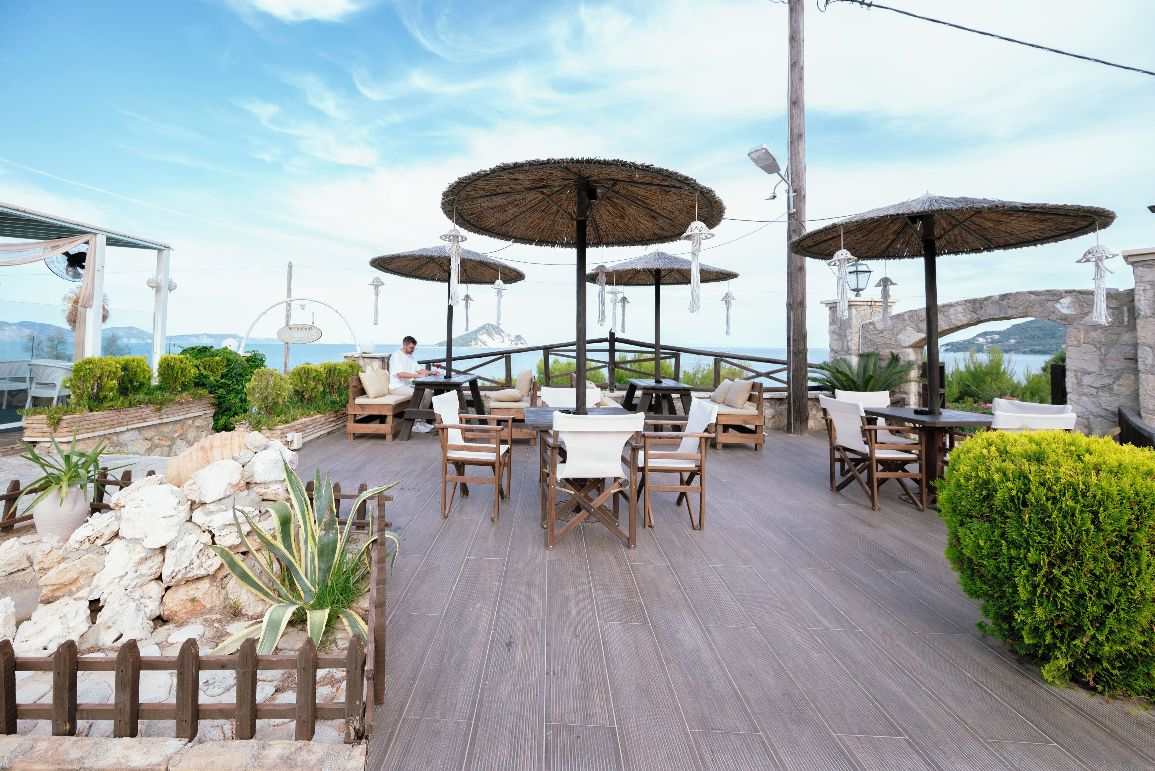 An outdoor patio with wooden tables and chairs, surrounded by stone walls and potted plants.