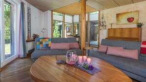 Una sala de estar acogedora con techo de madera, un ventanal grande, un sofá, una mesa de centro con velas y un cuadro en la pared.