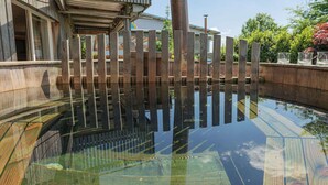 Vista clara de una piscina con listones de madera y fondo de cristal, rodeada por un suelo de hormigón y una valla metálica.