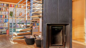 Un interior moderno con una escalera espiral, una chimenea y estanterías llenas de libros.
