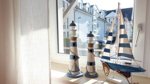 Een raam met twee scheepvaartbeeldjes en uitzicht op een woonwijk.