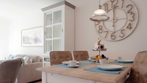 Een eetgedeelte met een houten tafel, stoelen, een grote wandklok en een kast.
