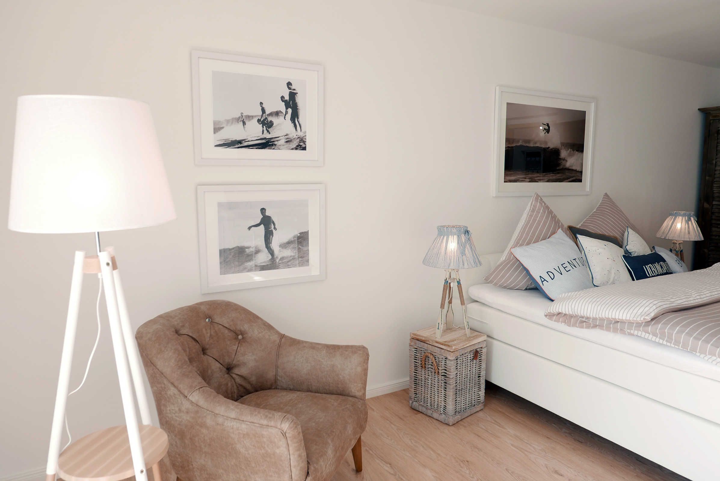 A bedroom with a bed, a chair, a lamp, and framed pictures on the wall.