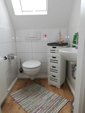 Ein kleines, modernes Badezimmer mit Toilette, Waschbecken, Stauraum und einem Oberlicht.