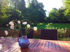 Et træbord med en vase blomster og udsigt til en grøn have.