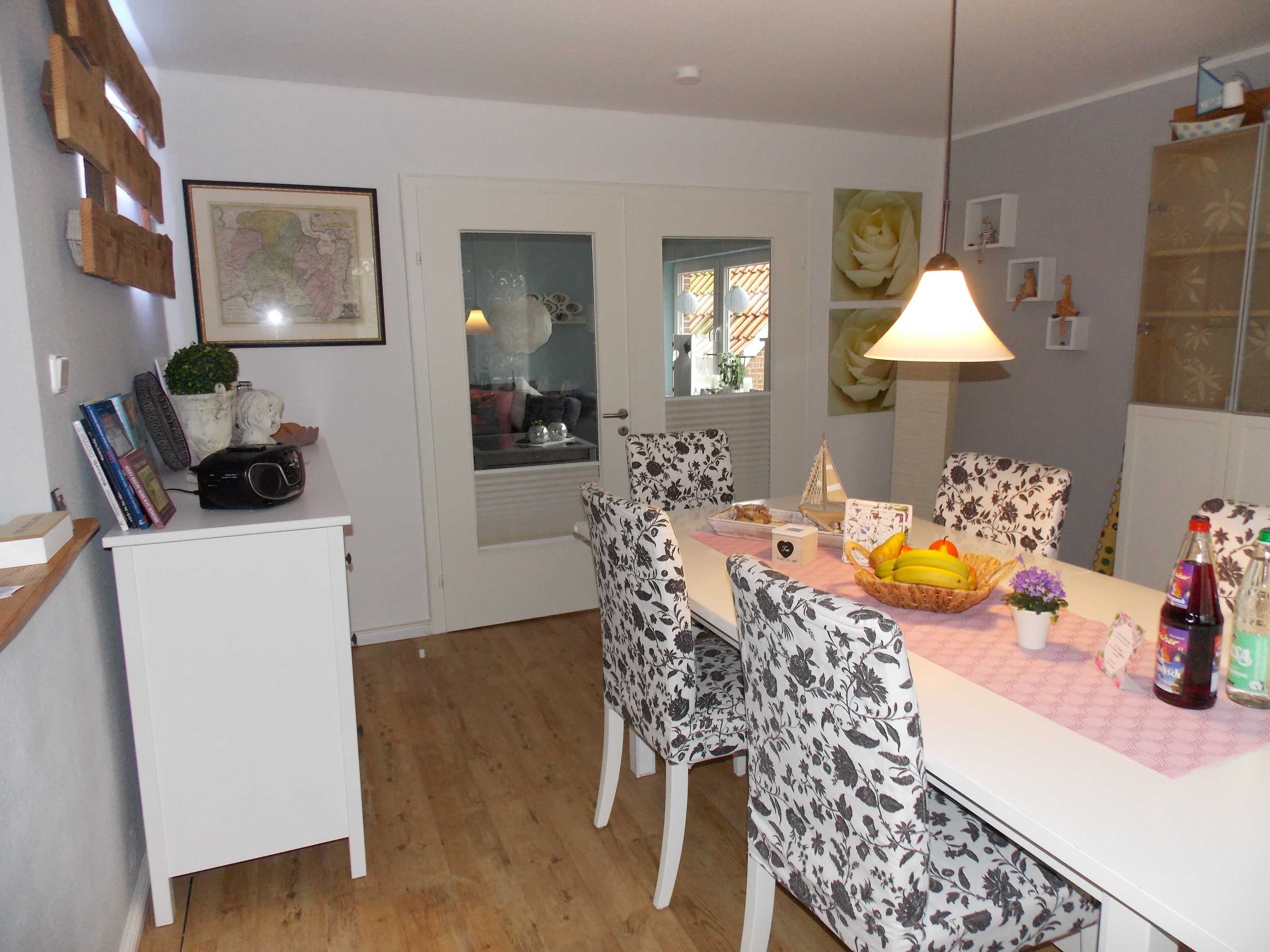 A dining area with a white table, patterned chairs, a fruit basket, and a bottle of wine.