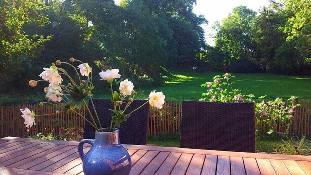 A wooden table with a vase of flowers and a view of a green garden.
