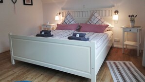 A bedroom with a bed, two bedside tables, a nightstand, a wall-mounted lamp, a heart-shaped decoration, and a small potted plant.