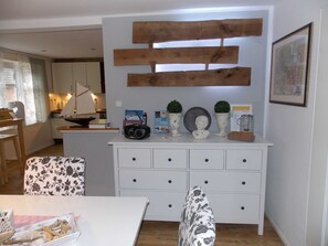 Un comedor con una mesa blanca, sillas estampadas, un armario blanco con cajones y un adorno de pared de madera.