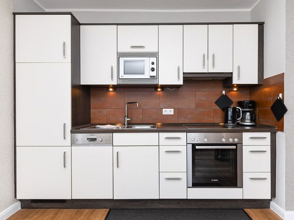 A modern kitchen with white cabinets, a Bosch microwave, a coffee maker, and an oven.