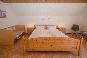 A bedroom with a wooden bed, a crib, two bedside tables with lamps, and a chair.