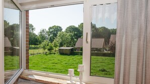 A room with a large window overlooking a green lawn and a wooden structure. - Vacation home Voß, 65260 - Holiday home in East Frisia, 130 sqm, 4 stars (Moormerland)