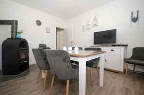 A modern living room with a fireplace, a dining table with chairs, a television, and a white cabinet.