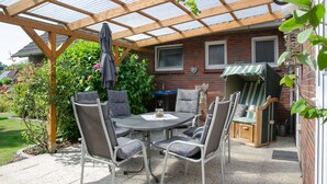 A covered patio area with a round table and chairs, a grill, and a clock on the wall. - Vacation home Voß, 65260 - Holiday home in East Frisia, 130 sqm, 4 stars (Moormerland)