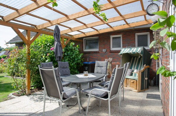 A covered patio area with a round table and chairs, a grill, and a clock on the wall.