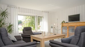 A modern living room with a sofa set, a wooden coffee table, and a flat-screen TV on a wooden cabinet. - Vacation home Voß, 65260 - Holiday home in East Frisia, 130 sqm, 4 stars (Moormerland)