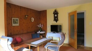 A room with a wooden wall, a sofa, a table, a TV, and a door. - Ferienwohnung bis 5 Personen (ca. 90 qm) (Kiefersfelden)