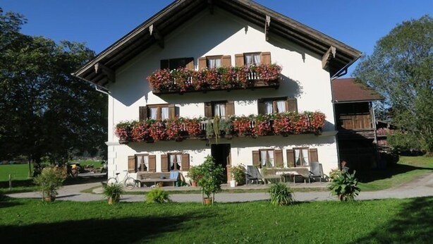 A two-story building with a balcony, surrounded by greenery and a clear sky. - Ferienwohnung bis 5 Personen (ca. 90 qm) (Kiefersfelden)