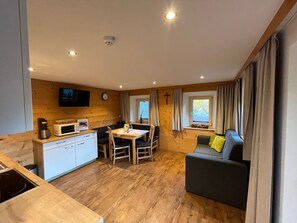 Een compacte kamer met een kitchenette, een eethoek, een bank en een aan de muur bevestigde televisie.