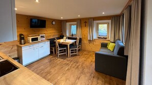 Una habitación compacta con kitchenette, zona de comedor, sofá y televisor montado en la pared.