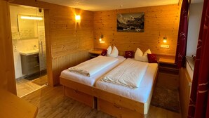 Una habitación de madera con una cama, un cuadro y un baño visible a través de una puerta de cristal.
