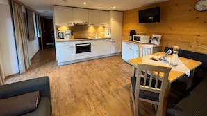Una cocina moderna con armarios blancos, microondas y cafetera. Hay una zona de comedor con una mesa y sillas.