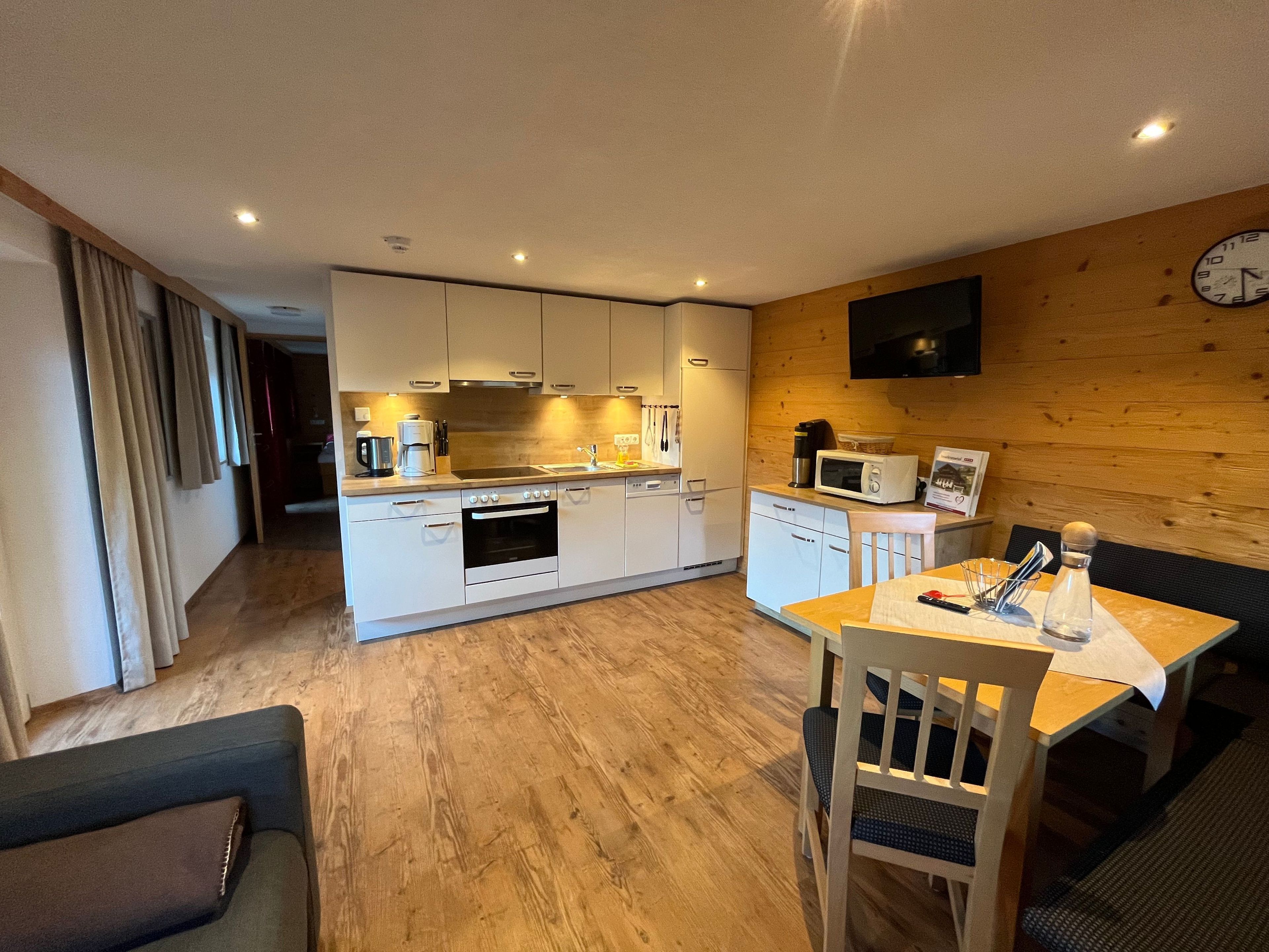A modern kitchen with white cabinets, a microwave, and a coffee maker. There is a dining area with a table and chairs.