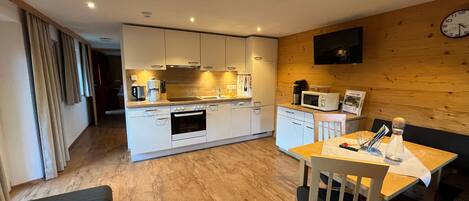 A modern kitchen with white cabinets, a microwave, and a coffee maker. There is a dining area with a table and chairs.